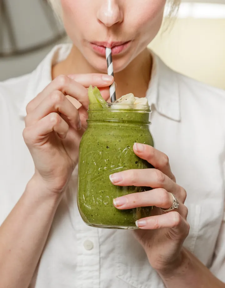Woman sipping a green smoothie through a striped straw from a glass jar